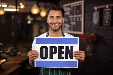 Smiling barista holding open sign in the bar